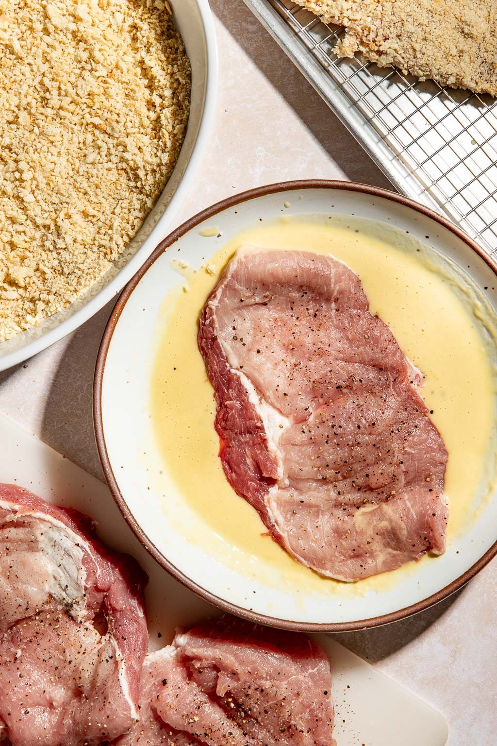 Pork being dipped into the egg/flour mixture before being breaded