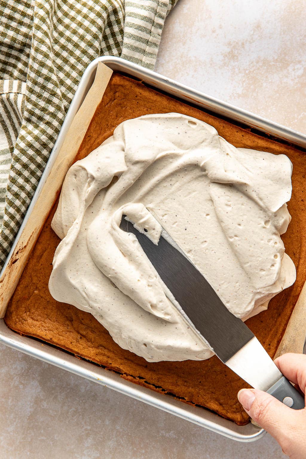 Stabilized whipped cream being spread over sweet potato pie bars. 