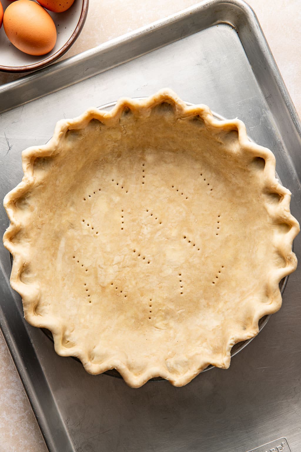 docked pie crust in a pie pan on a metal baking sheet
