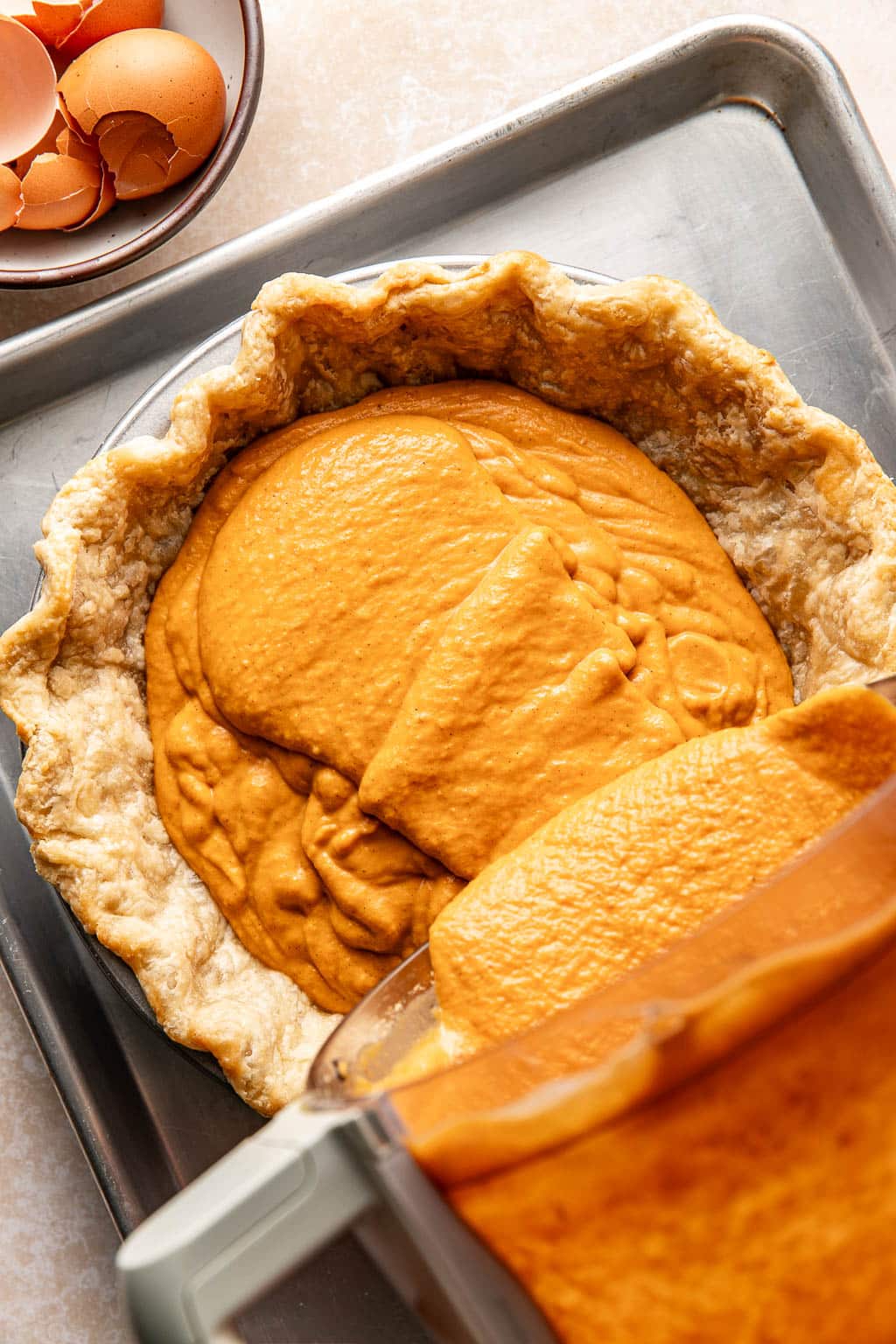 pumpkin pie filling being poured into a pie crust