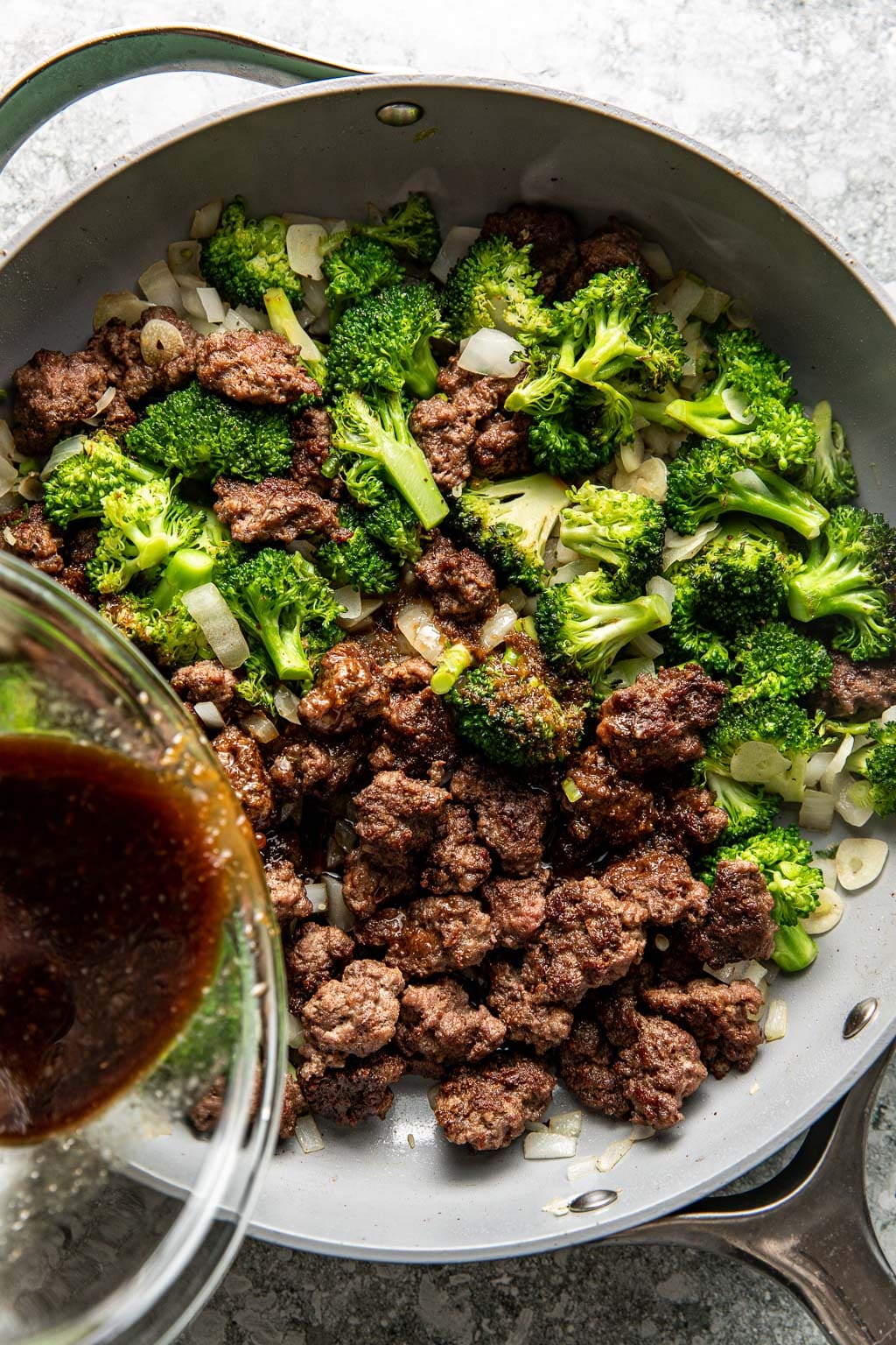 Ground beef and broccoli in a skillet with stir fry sauce being poured in
