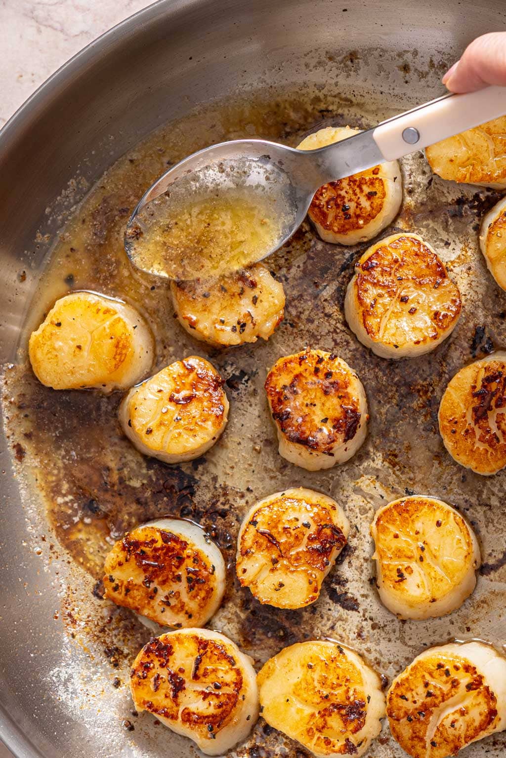 seared scallops in a skillet being basted with butter