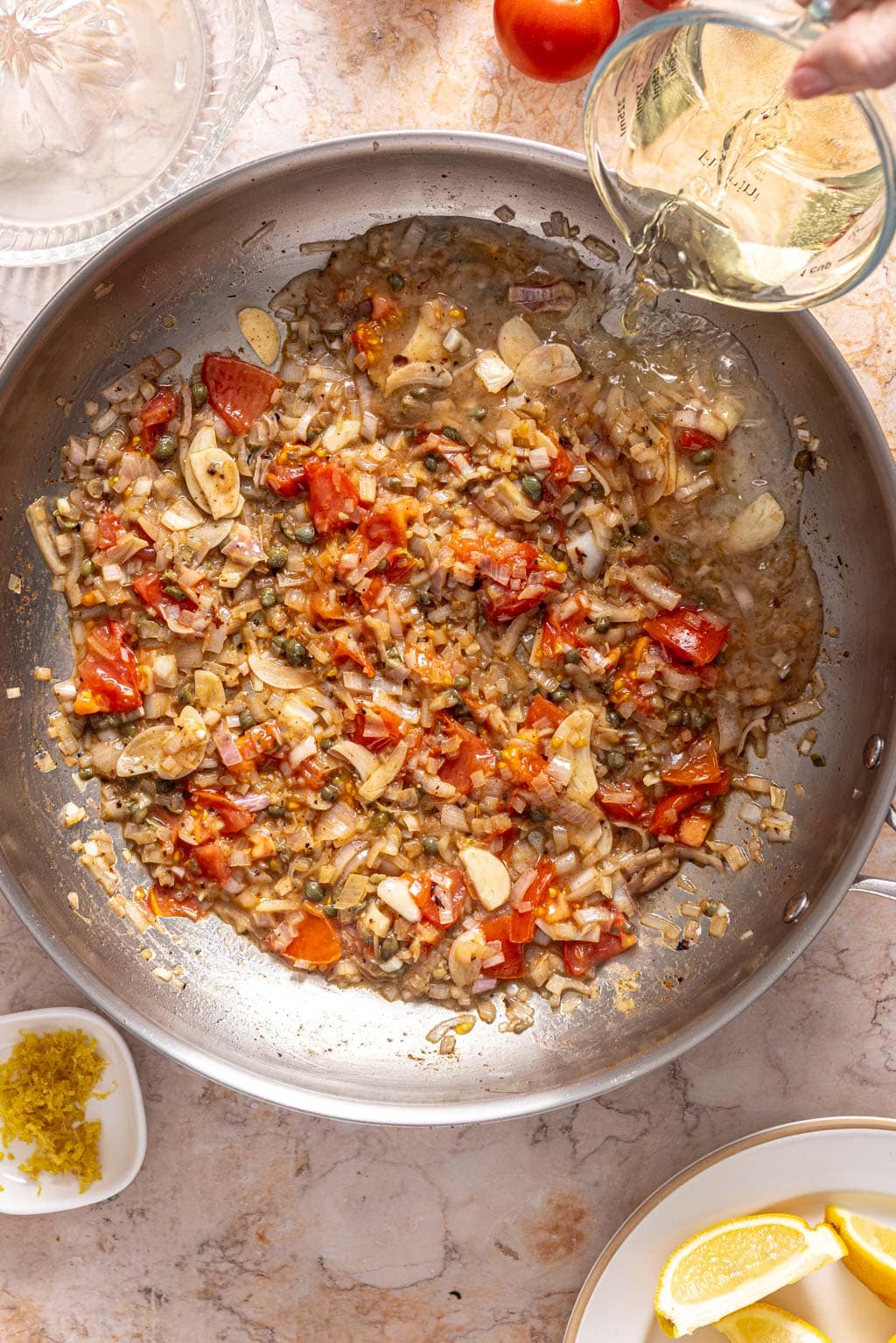 tomatoes, capers, and white wine being added to the pan sauce. 