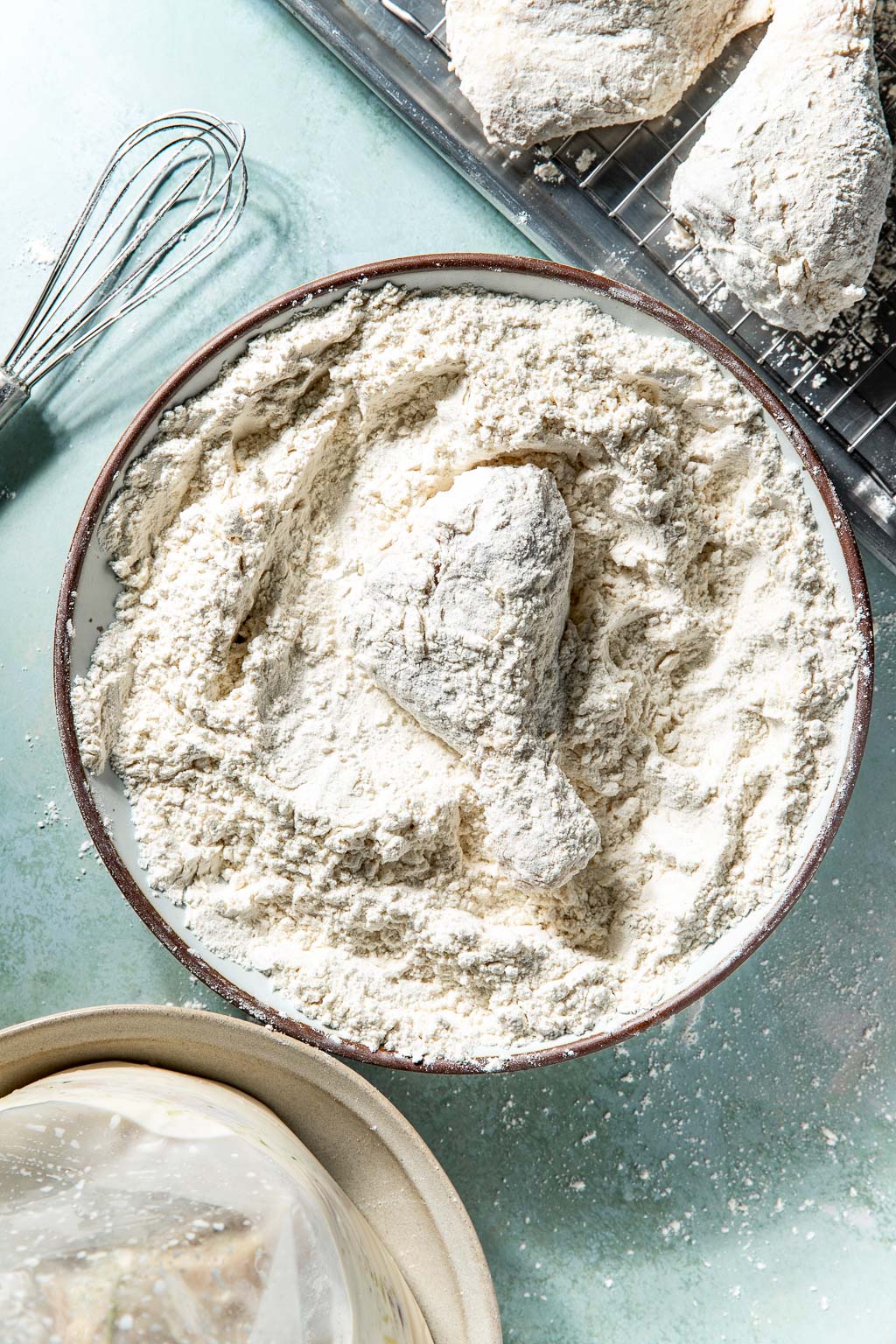 Chicken drumstick being dredged in a bowl of flour and cornstarch