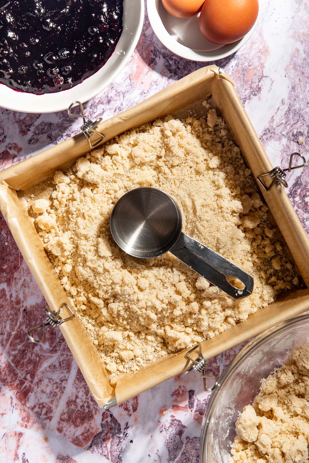 crust being pressed into a baking pan with a measuring cup