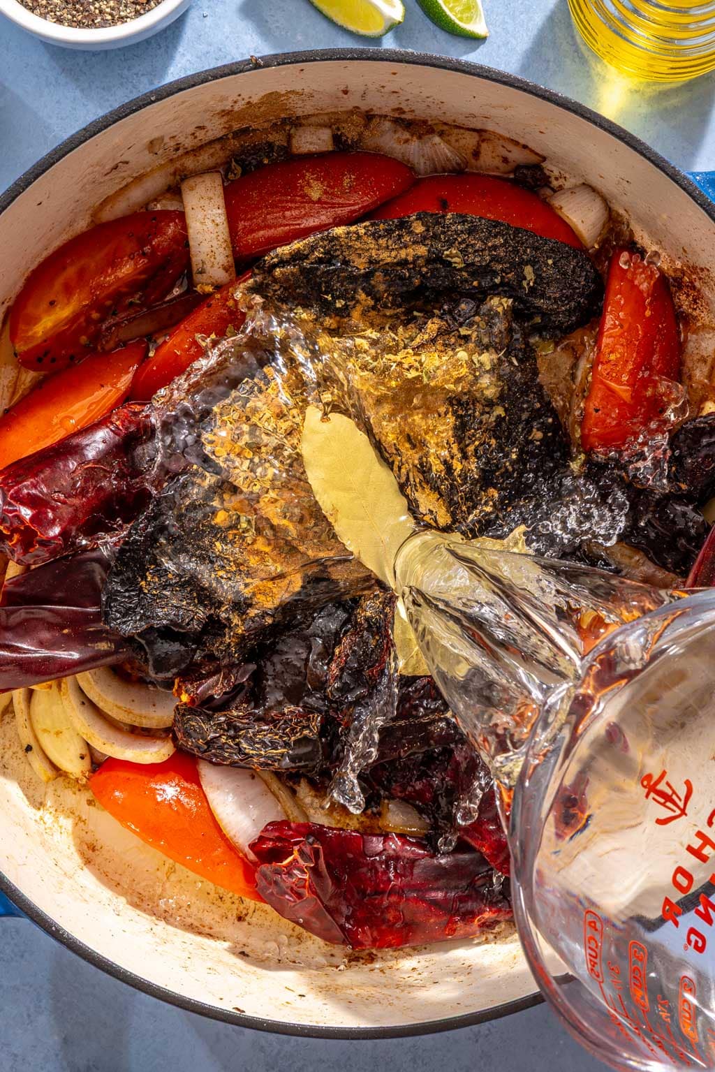 Dried chilies, spices, bay leaves, and water being added to the sautéed tomatoes and onions