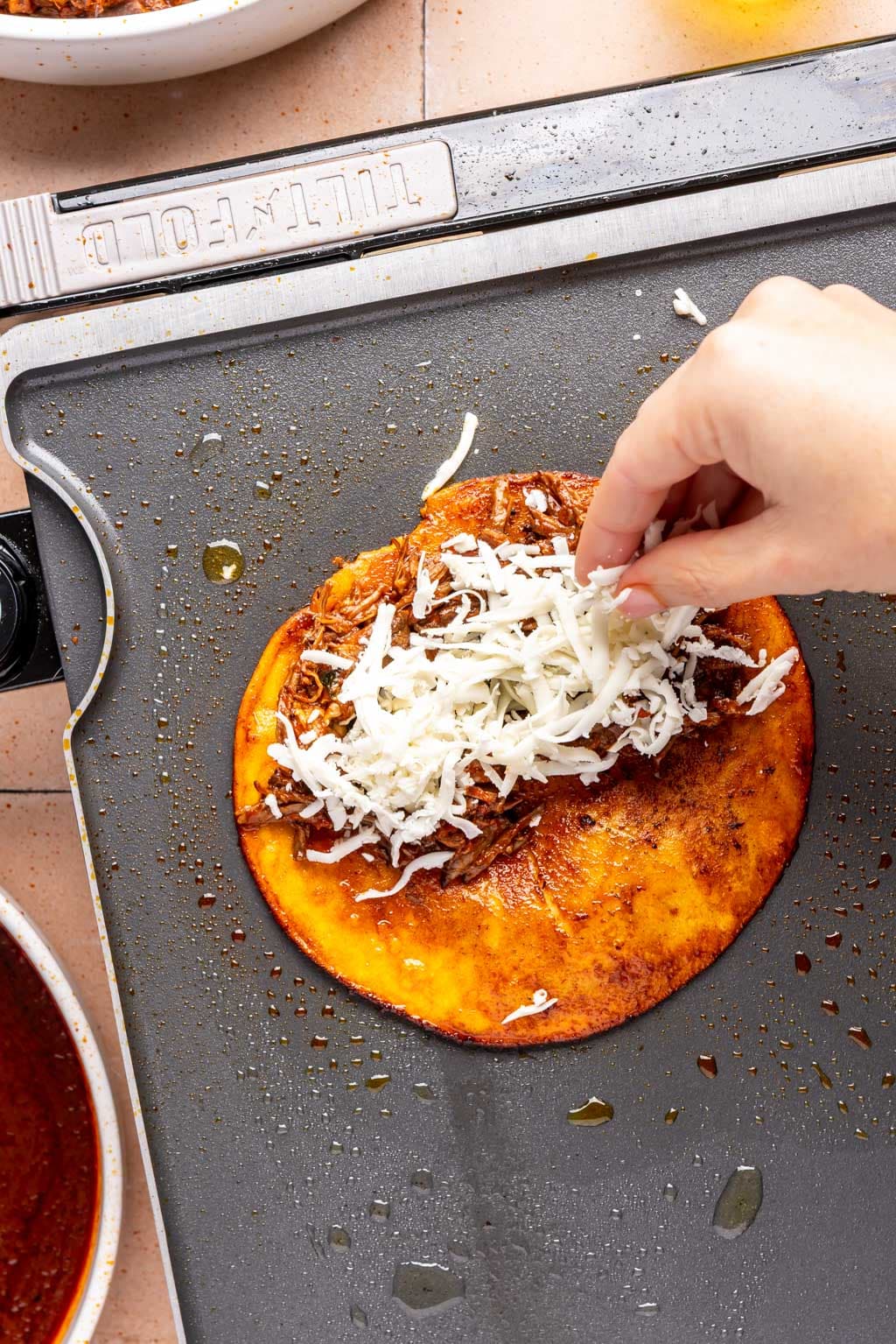 cheese and birria being added to the crispy tortilla