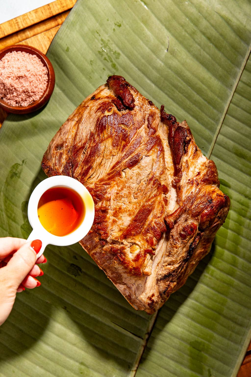 liquid smoke being poured over seared pork on banana leaves